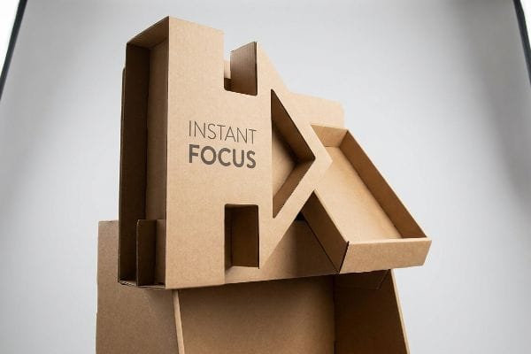 Expositor POP de cartón corrugado marrón, estructura troquelada en 3D, con el texto "Instant Focus", diseñado para la conversión en puntos de venta.