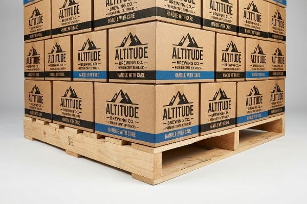 Brown corrugated boxes from Altitude Brewing Co., 'Premium Craft Beverages', 'Handle With Care', stacked on a wooden pallet.