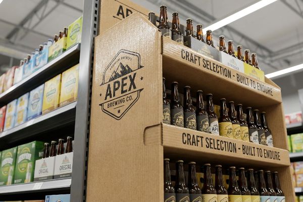 A corrugated retail display features Apex Brewing Co. craft beer bottles, labeled 