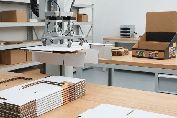 White and brown corrugated cardboard retail display components are precisely assembled by an automated packaging machine in a manufacturing facility.