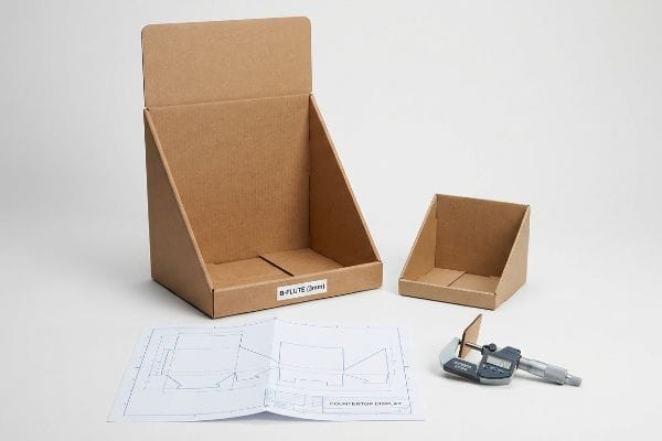 Brown B-Flute (3mm) corrugated cardboard countertop display boxes, with a dieline blueprint and a micrometer measuring material thickness.