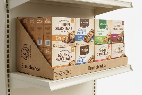 A retail shelf display by Bramobradea, custom printed, showcasing Jutinmues Gourmet Snack Bars and Gourmet Mounts in corrugated cardboard boxes.