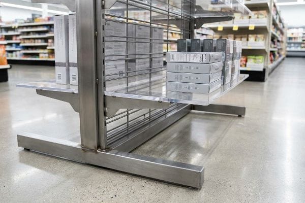 A durable brushed metal retail display features clear acrylic shelves stocked with light-colored product boxes in a grocery store aisle, highlighting a permanent POP fixture.
