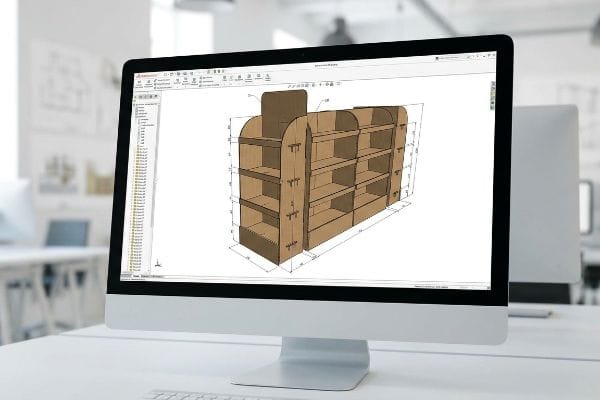 A computer monitor displays a 3D CAD model of a brown multi-shelf grocery store end cap display, showing design and dimensions for retail merchandising.