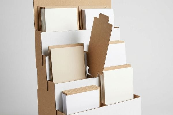 Brown corrugated cardboard card rack with tiered pockets, displaying stacks of blank white and beige cards using modular dividers.