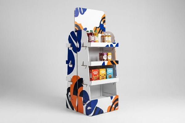 White cardboard floor display with abstract blue and orange patterns, showcasing various food products on three shelves.