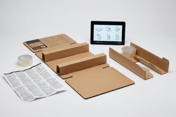 Brown corrugated cardboard components, tape, a printed manual, and a tablet showing visual assembly instructions.