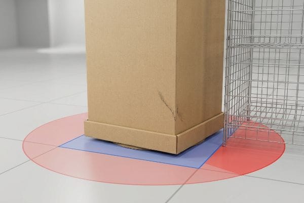 A large cardboard box on a blue square base with a red rotational sweep zone marked on a white tiled floor next to a wire rack, illustrating grid layout clearance.