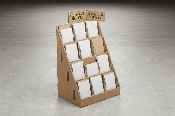 A brown cardboard tiered display stand showcases various white and light brown cards, with "Custom Card Solutions" signs at the top.