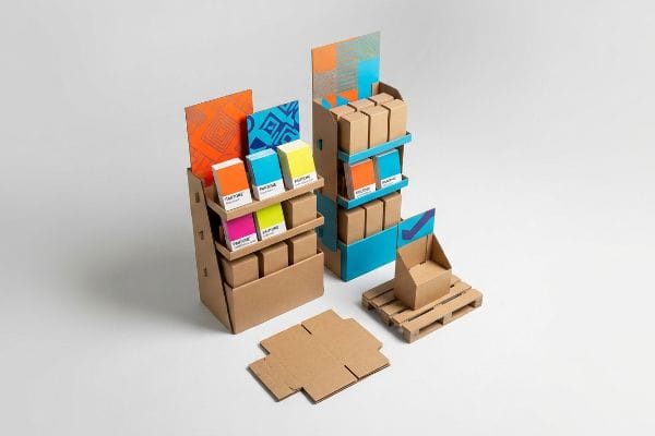 Temporary retail displays made of corrugated cardboard, showcasing Pantone color boxes in orange, blue, magenta, and yellow, with unassembled components.