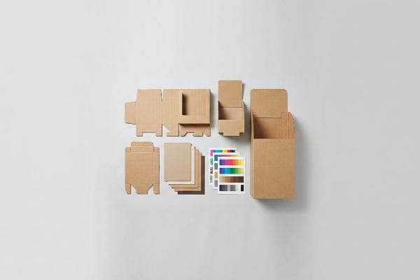 Various stages of custom cardboard display production, including flat die-cut sheets, partially assembled units, a finished brown display, and color swatches, are laid out.
