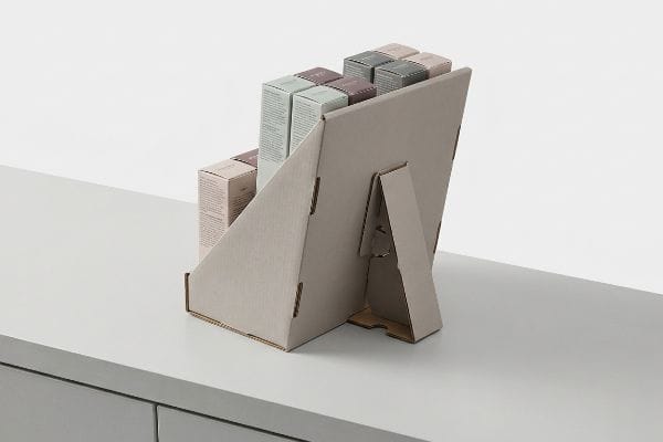 Cardboard Countertop Display Easel Beige cardboard countertop display with an extended easel back, showcasing pastel cosmetic product boxes on a grey counter.