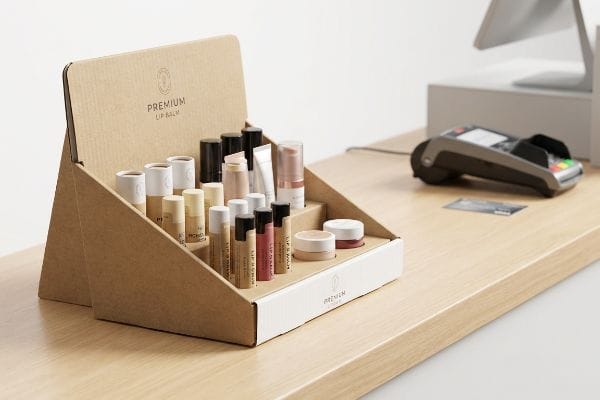 Natural brown corrugated cardboard countertop PDQ display with Premium Lip Balm products, featuring an extended easel back on a wooden counter.