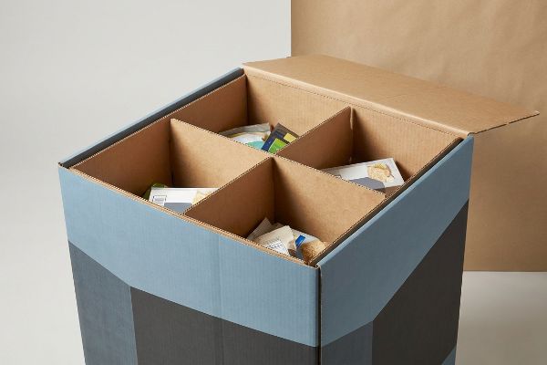 Cardboard display bin with internal H-dividers holding loose merchandise, featuring a blue-grey geometric pattern.