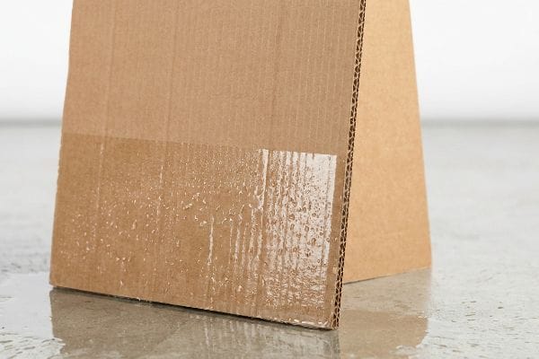 Brown corrugated cardboard box with clear poly-coat barrier on bottom 4 inches, showing water droplets for moisture defense.