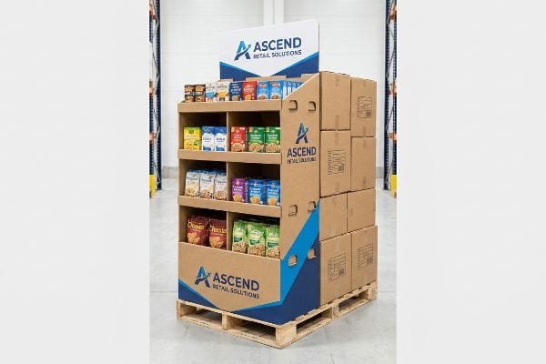 Un présentoir de point de vente en carton robuste d'Ascend Retail Solutions, conçu pour les conditions réelles d'un magasin, présentant des produits à plusieurs niveaux sur une palette en bois dans un entrepôt.