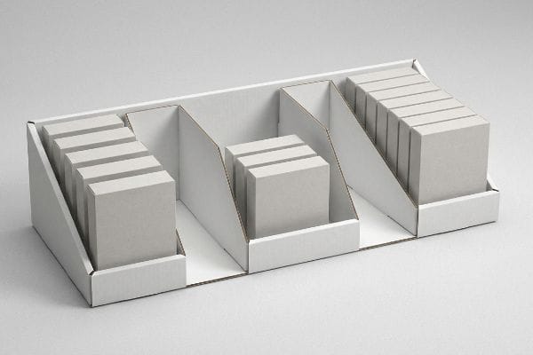 White corrugated cardboard display tray with three modular compartments holding stacks of products, showcasing strategic clearance buffers.