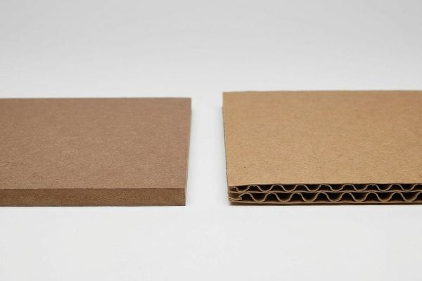 A flat brown chipboard piece sits beside a corrugated cardboard section, revealing its wavy fluted core for enhanced durability.