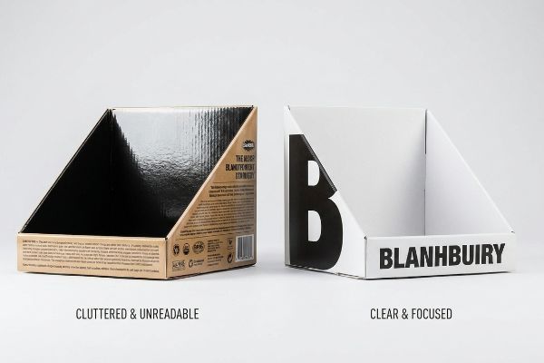 Bandejas de apresentação em cartão contrastantes: embalagem castanha com texto pequeno e acabamento brilhante, em contraste com embalagem branca, clara e objetiva, com o texto "Blanhbuiry" em negrito.