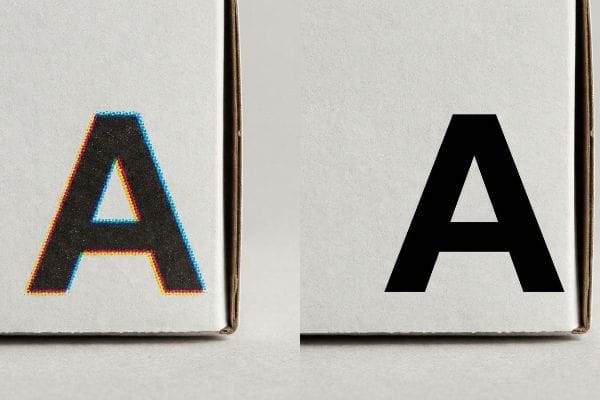 White cardboard surface shows a fuzzy CMYK 'A' with cyan and magenta fringes beside a razor-sharp, solid black spot color 'A'.