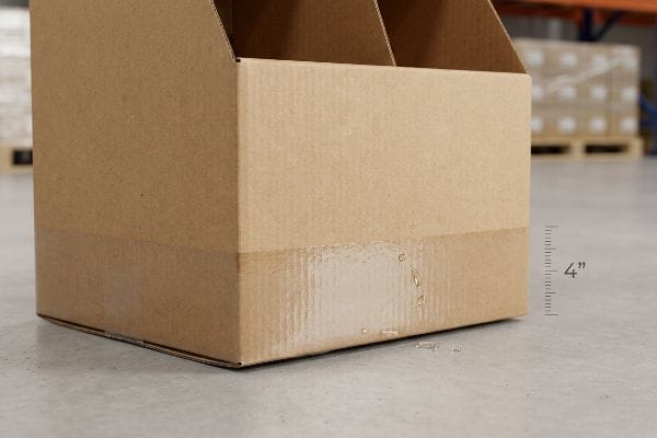 Corrugated cardboard display base with 4-inch moisture absorption from water, showing retail floor damage.