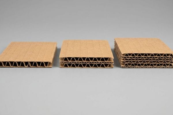 Brown corrugated cardboard samples display single-wall, double-wall, and triple-wall structures, revealing distinct fluted layers on a gray surface.