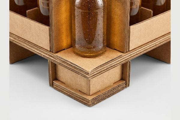 A robust, multi-layered corrugated cardboard beverage display securely holds a glass bottle with amber liquid and condensation.