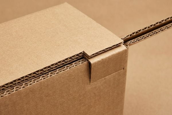 Close-up of a corrugated cardboard interlocking tab and slot, revealing visible E-flute layers and material caliper for proper assembly.