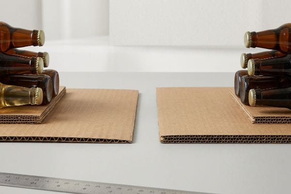 Corrugated cardboard sheets support amber glass bottles, illustrating packaging strength for heavy liquid goods.