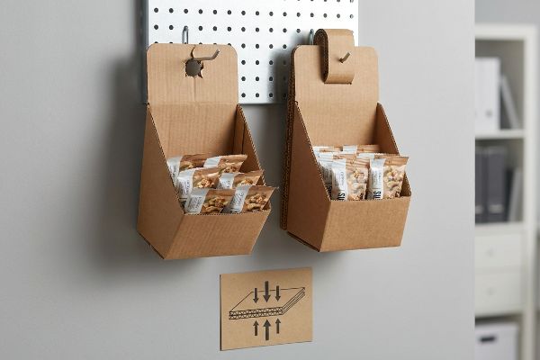 Brown corrugated sidekick displays on a pegboard, one with a reinforced double-layer spine, filled with snack pouches, next to a corrugated compression diagram.