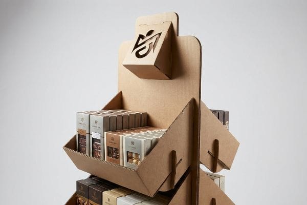 Natural brown corrugated cardboard POP display with a prominent die-cut logo, featuring tiered shelves of packaged chocolates.