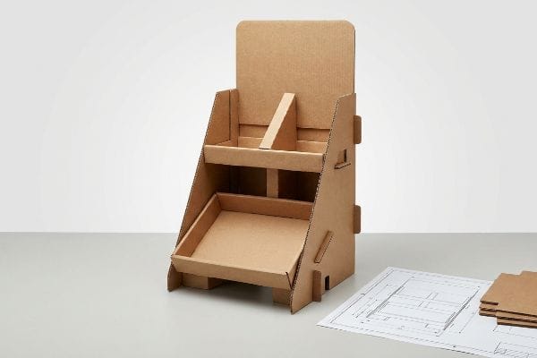 An unassembled two-tier corrugated cardboard POP display stand and its dieline blueprint are displayed, emphasizing bare structural design.