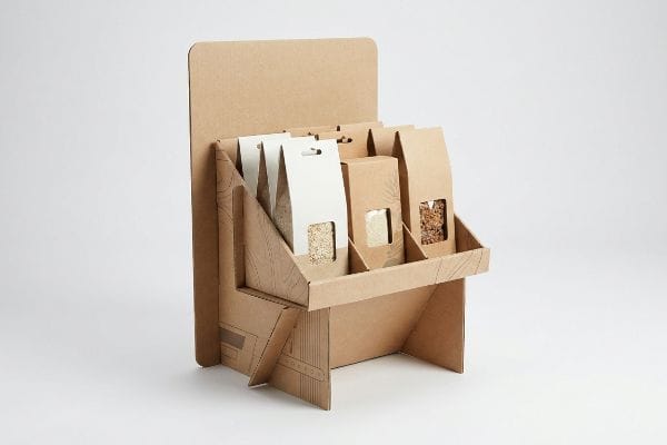 Brown corrugated cardboard POP display holds kraft and white pouches with visible grains and granola.