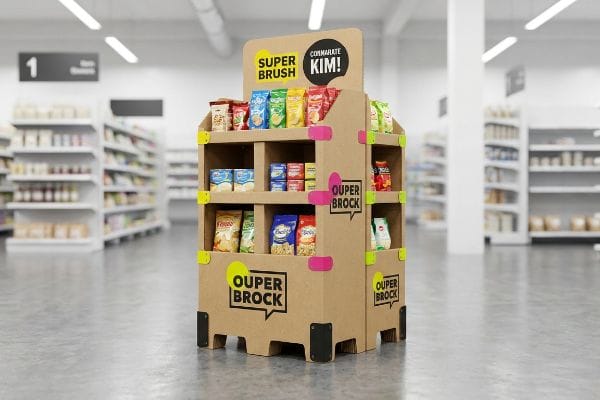 Un robusto expositor de punto de venta de cartón corrugado, con las marcas Super Brush y Ouper Brock, con detalles estructurales en rosa brillante y amarillo, que muestra diversos productos envasados ​​en un entorno minorista, con el lema "¡Comunícate con Kim!".