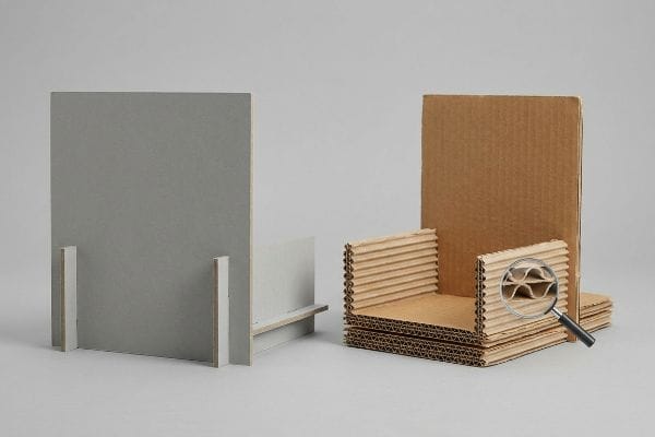 Visual comparison of grey chipboard and brown corrugated cardboard structures, with a magnifying glass revealing the internal flutes.