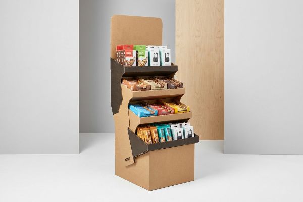 A brown corrugated POP retail display, made from layered paperboard, showcasing various packaged snacks on four tiers with dark brown accents.