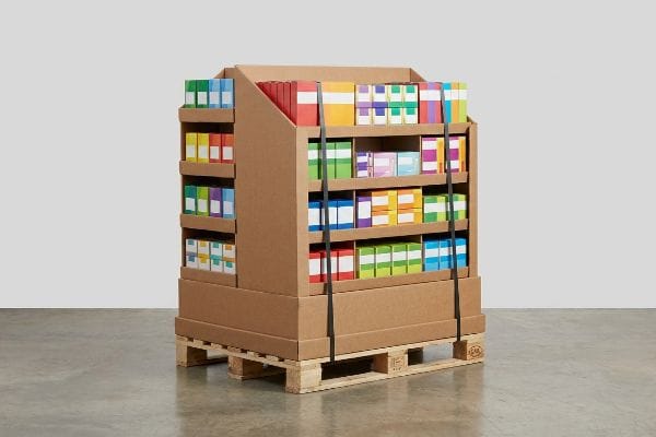 Brown corrugated cardboard fractional pallet display filled with colorful product boxes, secured with black straps on a wooden shipping pallet.