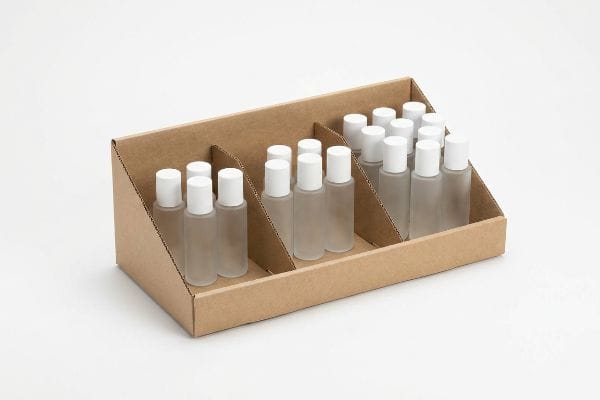 Brown corrugated cardboard display with modular dividers holding frosted plastic bottles and white caps, demonstrating asymmetrical grouping.