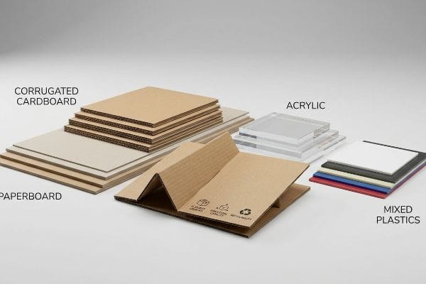 Various POP display materials, including Corrugated Cardboard, Paperboard, Acrylic, and Mixed Plastics, are arranged on a white surface.