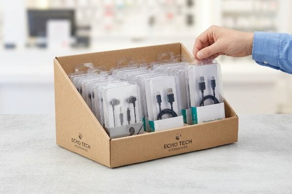 A hand reaches for a blister-packed Echo Tech charging cable in a corrugated cardboard PDQ display filled with earphones and cables.