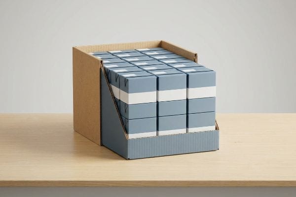 Um expositor PDQ pronto para venda, feito de papelão ondulado, exibe caixas azul-claras com listras brancas sobre um balcão de madeira.