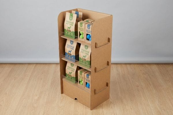 A corrugated cardboard display stand showcases Premium Pet Care bags and Organic Treats boxes with pet toys on three shelves.