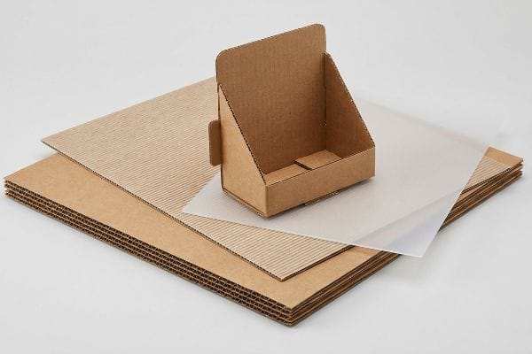 A small, empty corrugated cardboard POP display stand with stacks of brown paperboard sheets and a translucent material, showcasing packaging options.