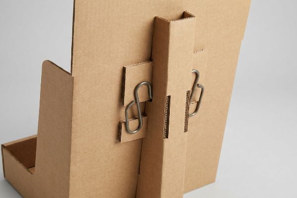 Natural kraft corrugated cardboard back panel with two metal S-clips securing a reinforced double-wall spine for a hanging merchandiser.