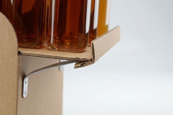 A sturdy metal bracket supports a corrugated cardboard shelf holding amber glass bottles, demonstrating sidekick display strength for liquid products.