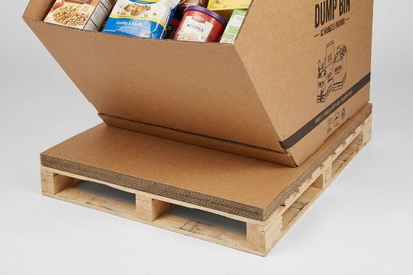 Protection des palettes pour bennes basculantes Feuille de glissement ondulée multicouche supportant un bac de déchargement brun rempli de produits sur une palette en bois, empêchant la déformation du niveau inférieur.