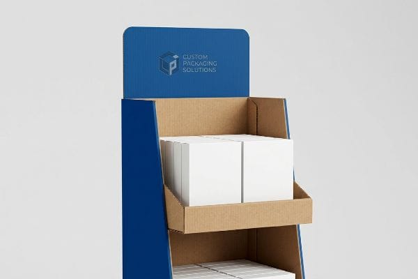 Expositor de papelão ondulado azul para ponto de venda, com a marca Custom Packaging Solutions, exibindo caixas de produtos brancas em prateleiras marrons.