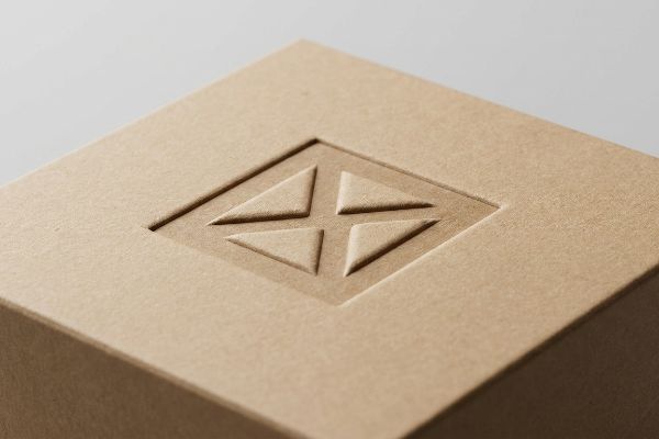 Brown kraft paperboard with a deeply debossed square containing four recessed triangular shapes, highlighting tactile packaging finish.
