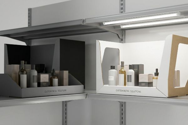 Two retail shelf displays, one gray and one white, feature products and 'Custom Retail Solutions' text. The white display has structural side windows and bright inner liners for product visibility.