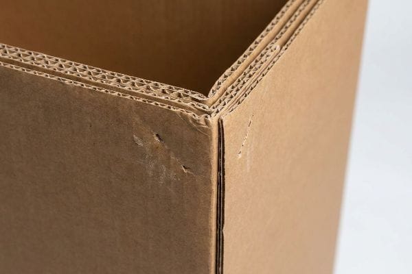 Close-up view of a brown double-wall corrugated cardboard box corner, highlighting its visible fluting layers and structural integrity.
